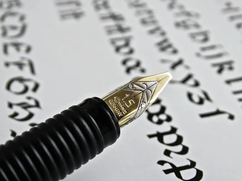 Detailed shot of a gold fountain pen nib on paper with calligraphy.
